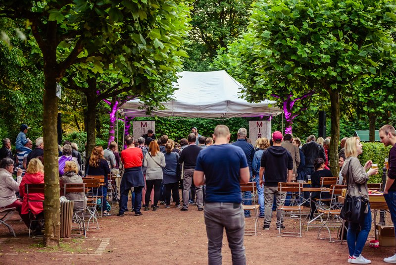 Veranstaltung im Biergarten der Freilichtbühne Wattenscheid. Im Hintergrund ist eine kleine Bühne zu sehen, davor stehen Menschen.