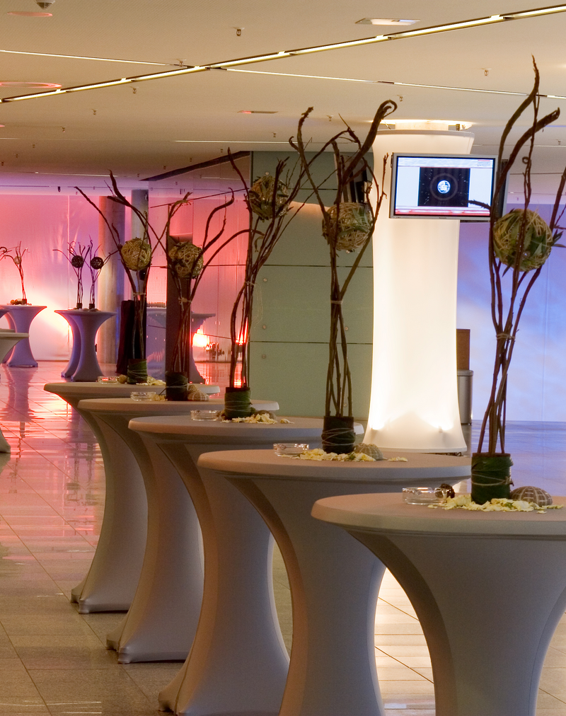 Festively decorated bar tables line the foyer on the first floor of the RuhrCongress Bochum. In the background, a screen is mounted on a column.